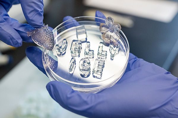 A petri dish with jelly ice that spells its name, being held by gloved hands