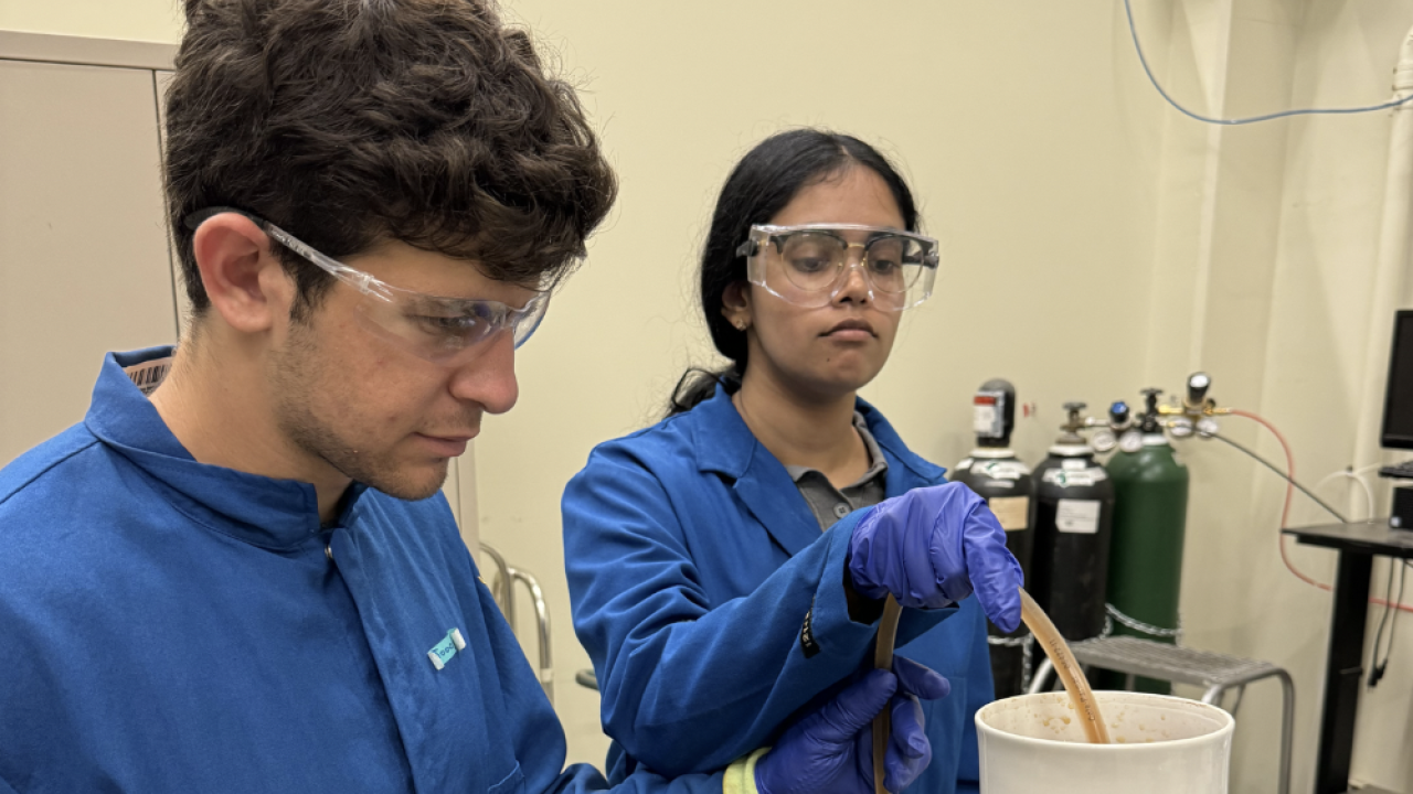 Two students in blue lab uniforms filtrating a substance
