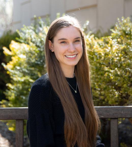 Morgan Johnson sits on a bench in front of yellow and green flowers