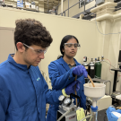 Two students in blue lab uniforms filtrating a substance