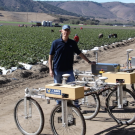 Stavros Vougioukas poses near robotic technology next to a field